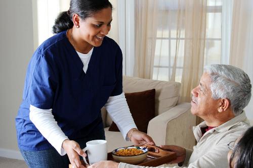 A carer bringing lunch to an elderly man